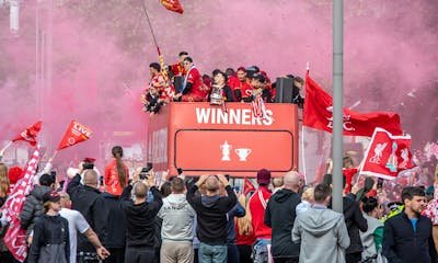 Celebratory parade in Liverpool with jubilant fans and players on an open-top bus.