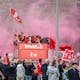 Celebratory parade in Liverpool with jubilant fans and players on an open-top bus.