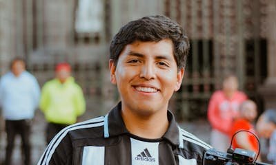 Smiling young man with camera tripod standing outdoors in casual attire.